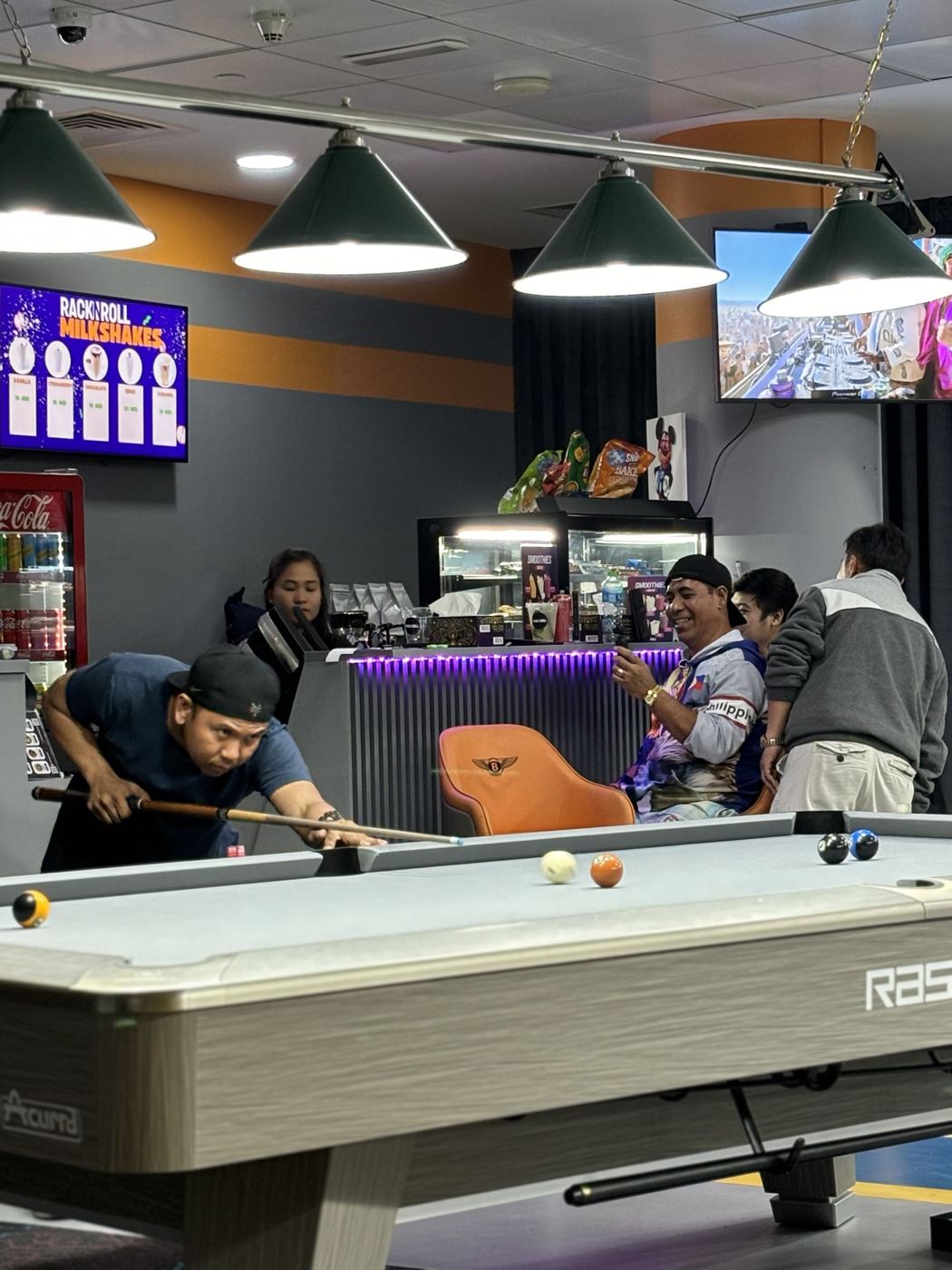 The pool hall with six tables under green lamps